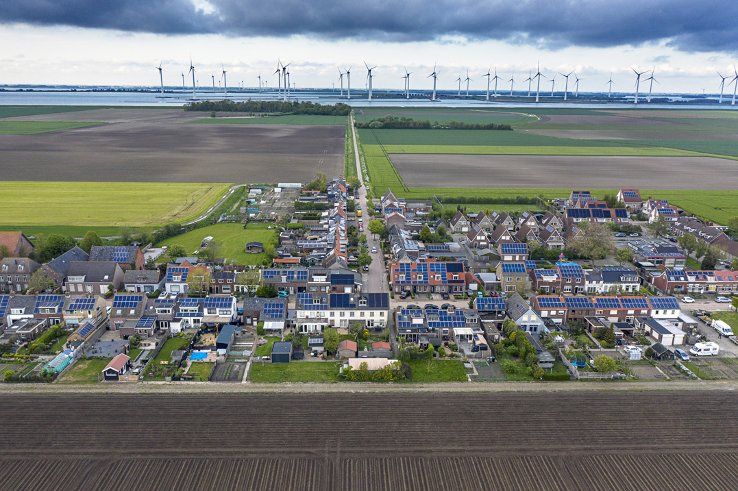 Foto bij het nieuwsbericht, dorp in Zeeland met zonnepanelen op de daken en windmolens in de verte.